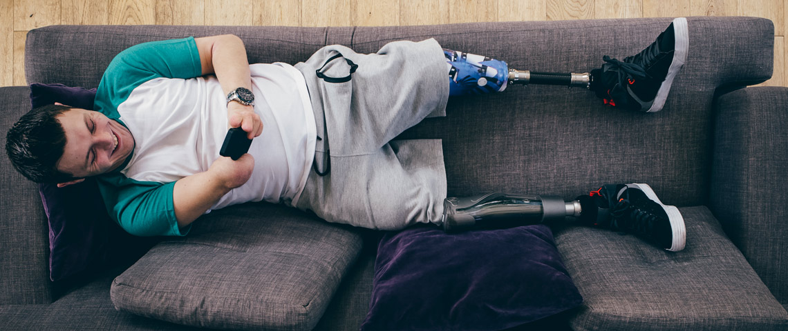 Mann med benproteser ligger i en sofa sett ovenfra